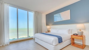A bedroom with a large window, a bed, two bedside tables, and a wall-mounted artwork.