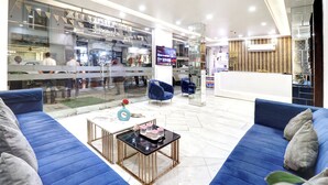 Una hall moderna con divani blu, un tavolino da caffè e una parete divisoria in vetro che separa l'area relax dal negozio.