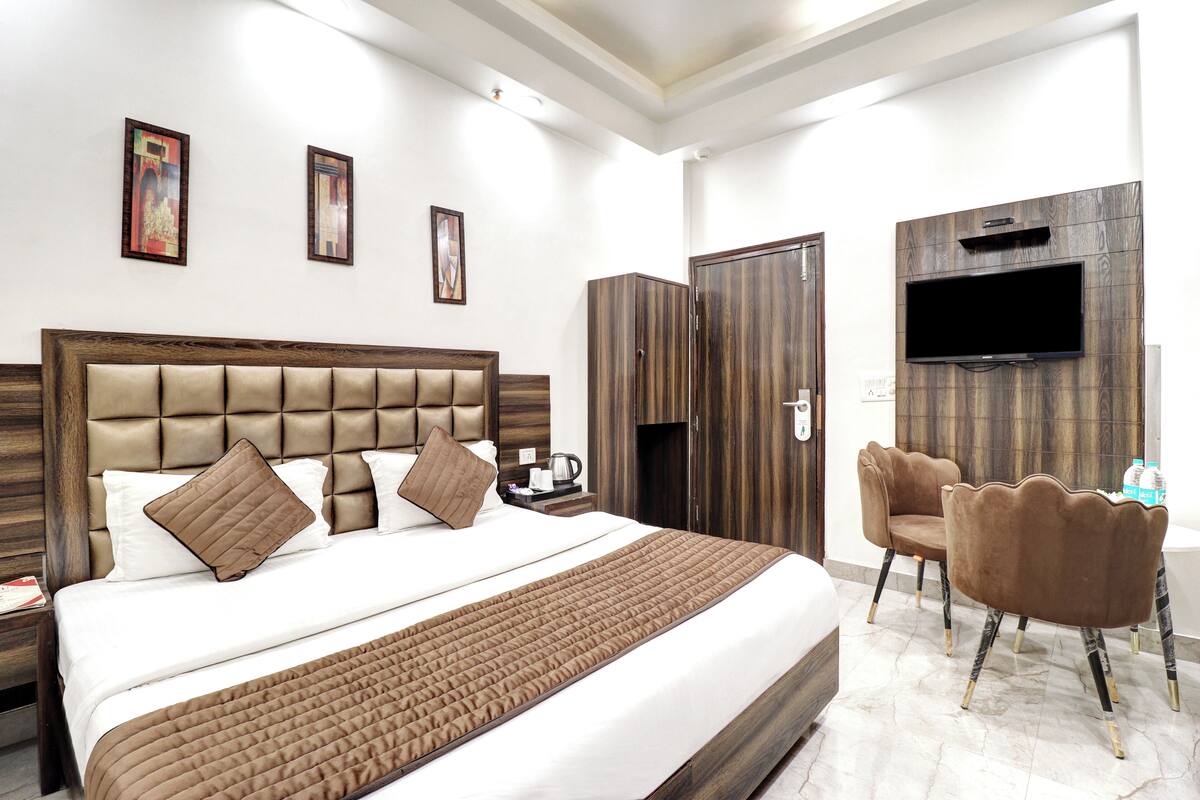 Une chambre d’hôtel avec un grand lit, un téléviseur fixé au mur et un coin salon avec des fauteuils.