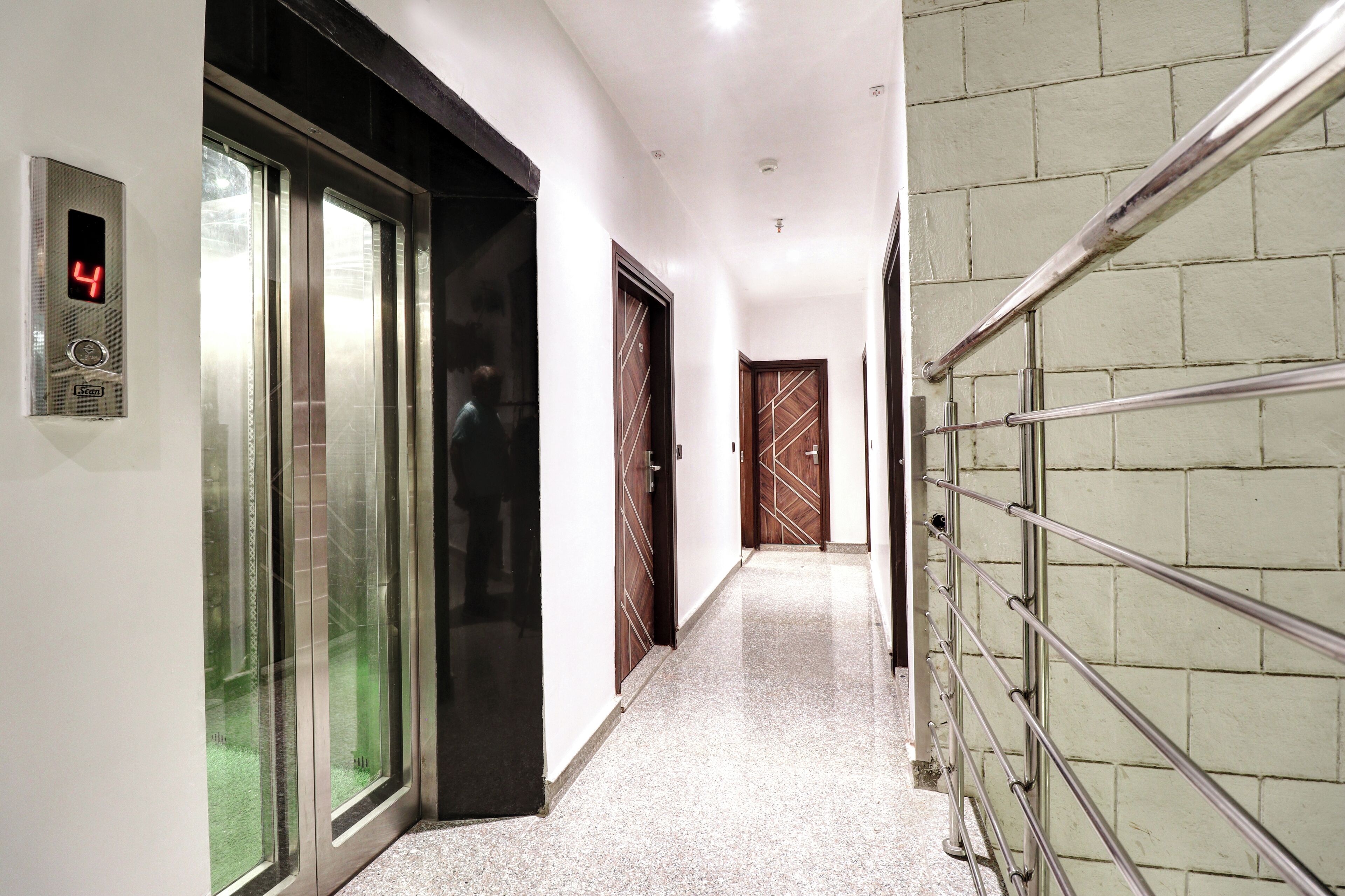 Um corredor com elevador de vidro, corrimão de metal e portas de madeira.