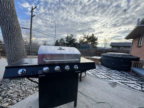 Ein Char-Broil Gasgrill mit vier Brennern und einem Edelstahl-Deckel, platziert auf einer Beton-Terrasse mit einem gemusterten Teppich.