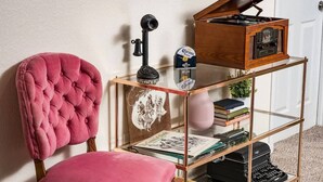 A room with a tufted pink chair, a glass-fronted wooden bookcase with books and a vintage radio, and a small table with a decorative item. - Hot Tub, Entertainers Lounge, 6 bedrooms - Denver's Beer Inspired BnB (westminster)