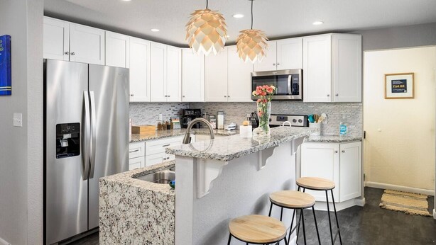 A modern kitchen with white cabinets, stainless steel appliances, a granite countertop, and a central island with stools. - Hot Tub, Entertainers Lounge, 6 bedrooms - Denver's Beer Inspired BnB (westminster)
