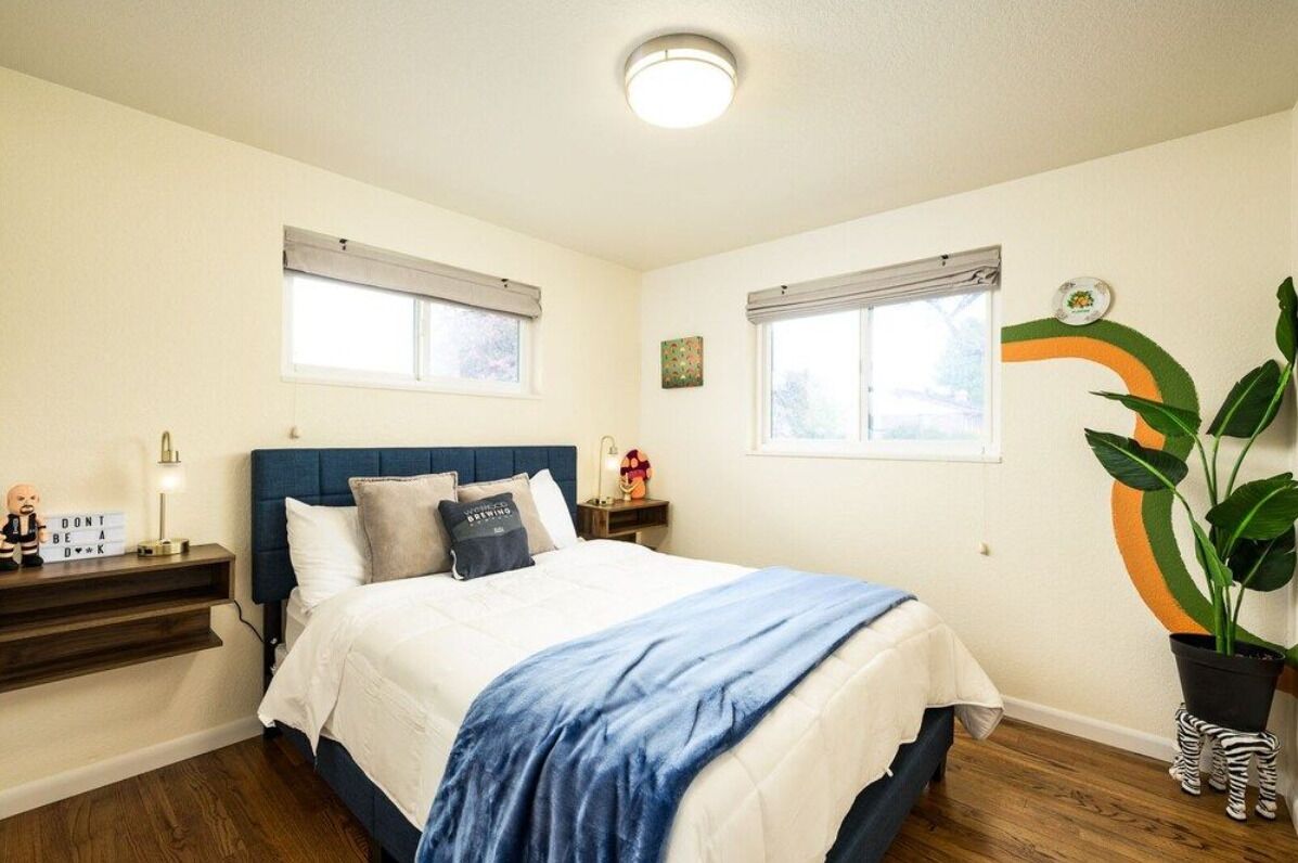 A bedroom with a bed, nightstands, a potted plant, and a wall decoration.