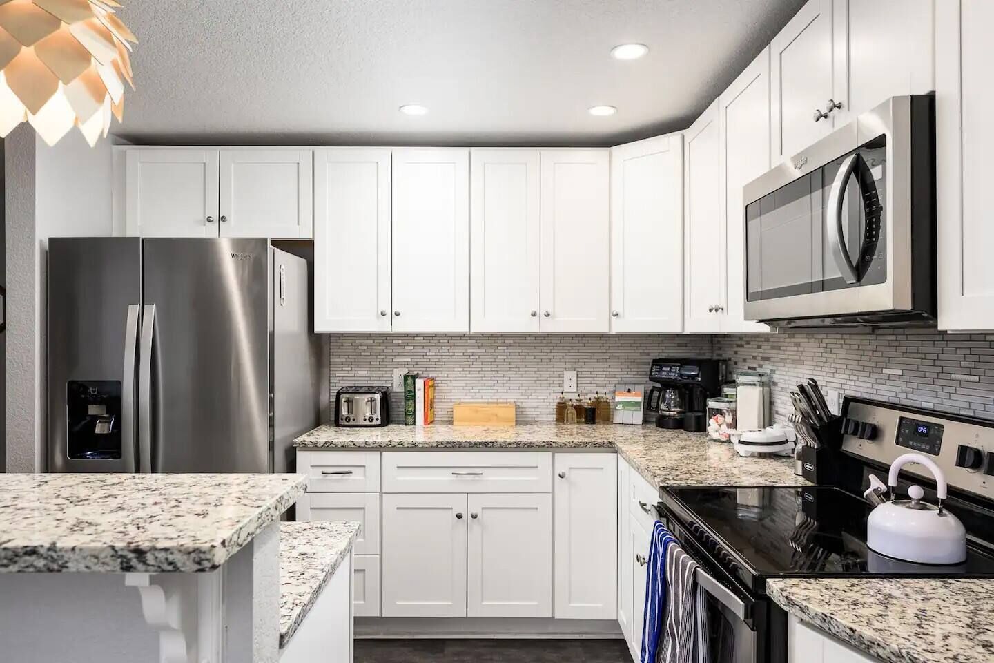 A modern kitchen with white cabinets, stainless steel appliances, granite countertops, and a backsplash.