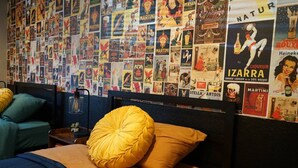 A hotel room with a bed featuring a yellow pillow, a wooden headboard, and a blue bedspread. The wall is decorated with vintage posters of various brands. - Hot Tub, Entertainers Lounge, 6 bedrooms - Denver's Beer Inspired BnB (westminster)