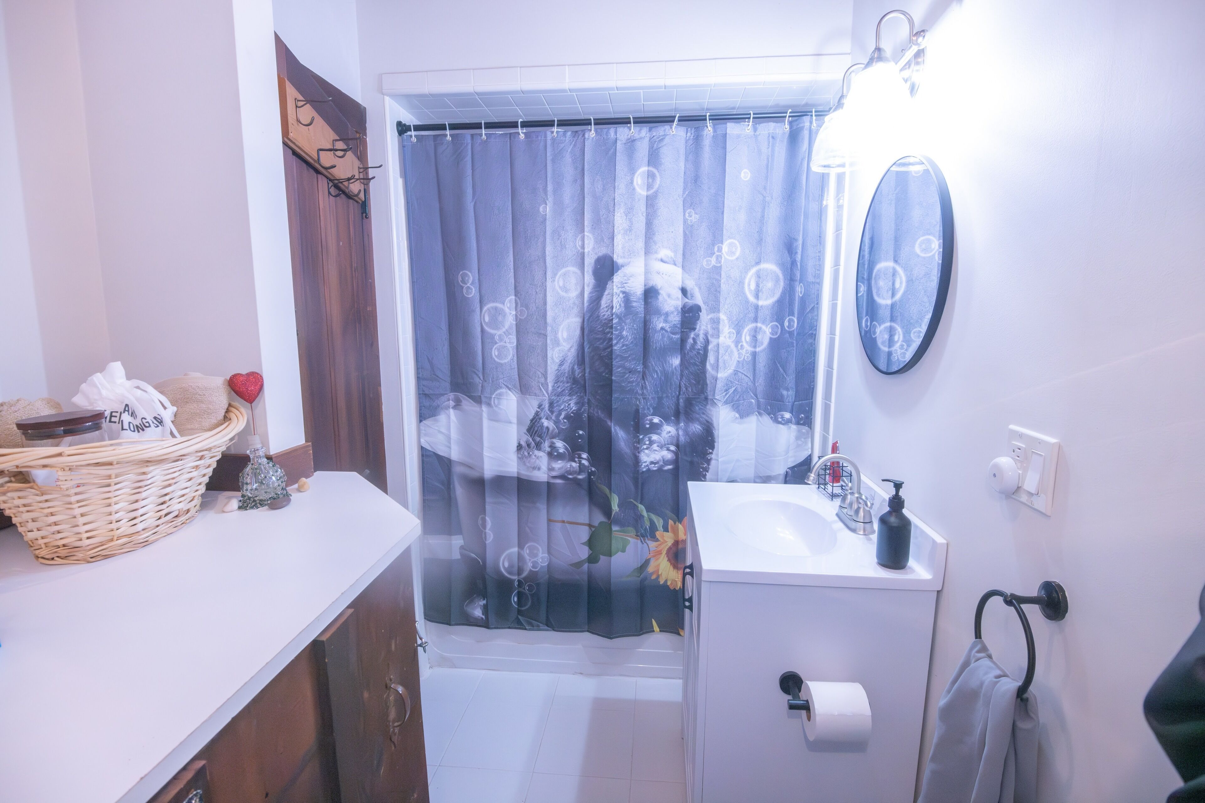 Un baño con cortina de ducha con diseño de oso, un lavamanos blanco con dispensador de jabón y un espejo sobre el lavamanos.