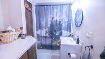 Un baño con cortina de ducha con diseño de oso, un lavamanos blanco con dispensador de jabón y un espejo sobre el lavamanos.