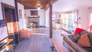 A cozy living room with a fireplace, wooden beams, a sofa, and a dining area.