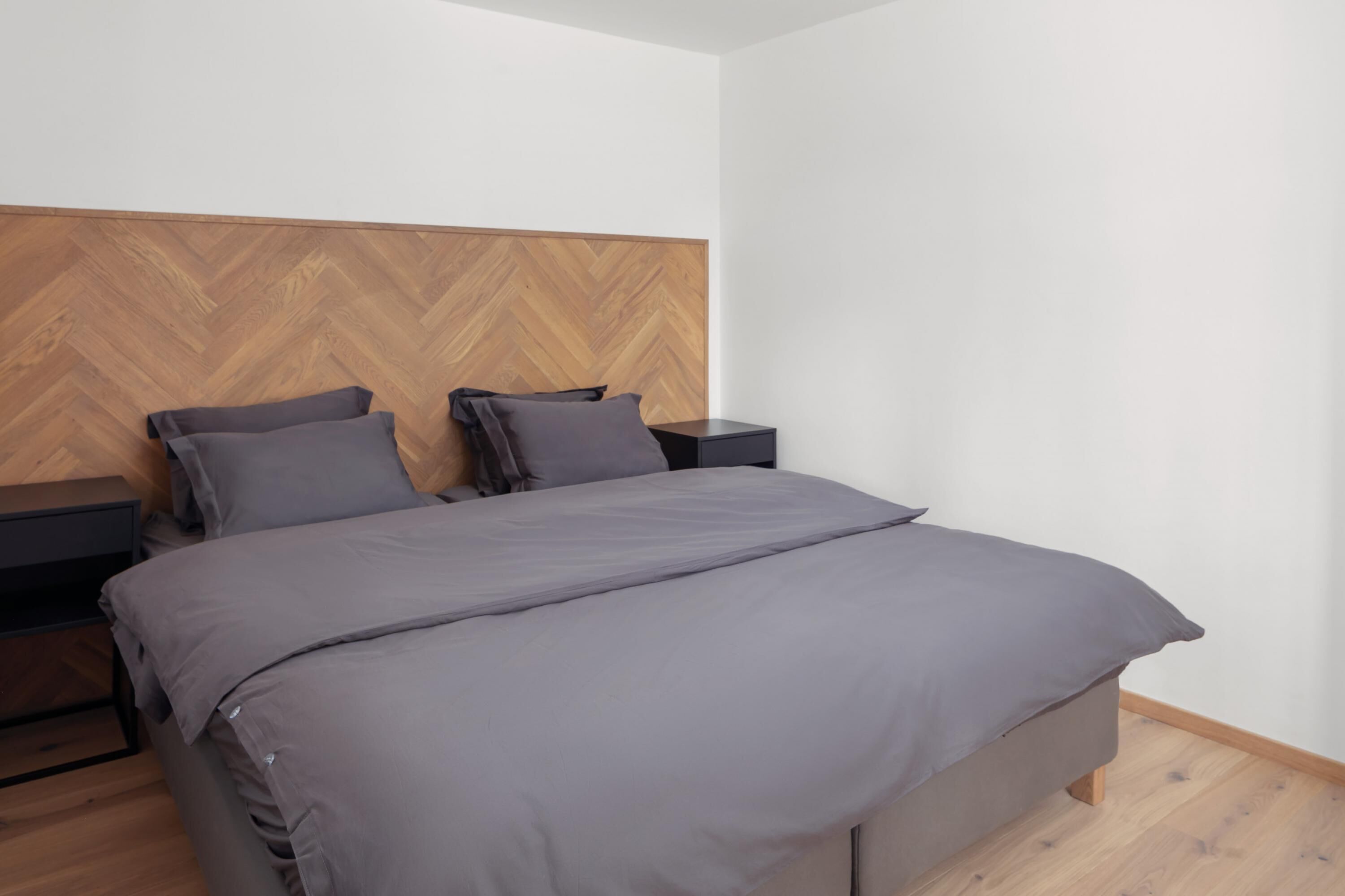 Une chambre moderne avec une tête de lit en bois à motifs en chevrons, un grand lit avec une literie grise et deux tables de chevet.