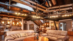 Een rustiek interieur met houten balken, leren banken, een houten salontafel en een keukenhoek.