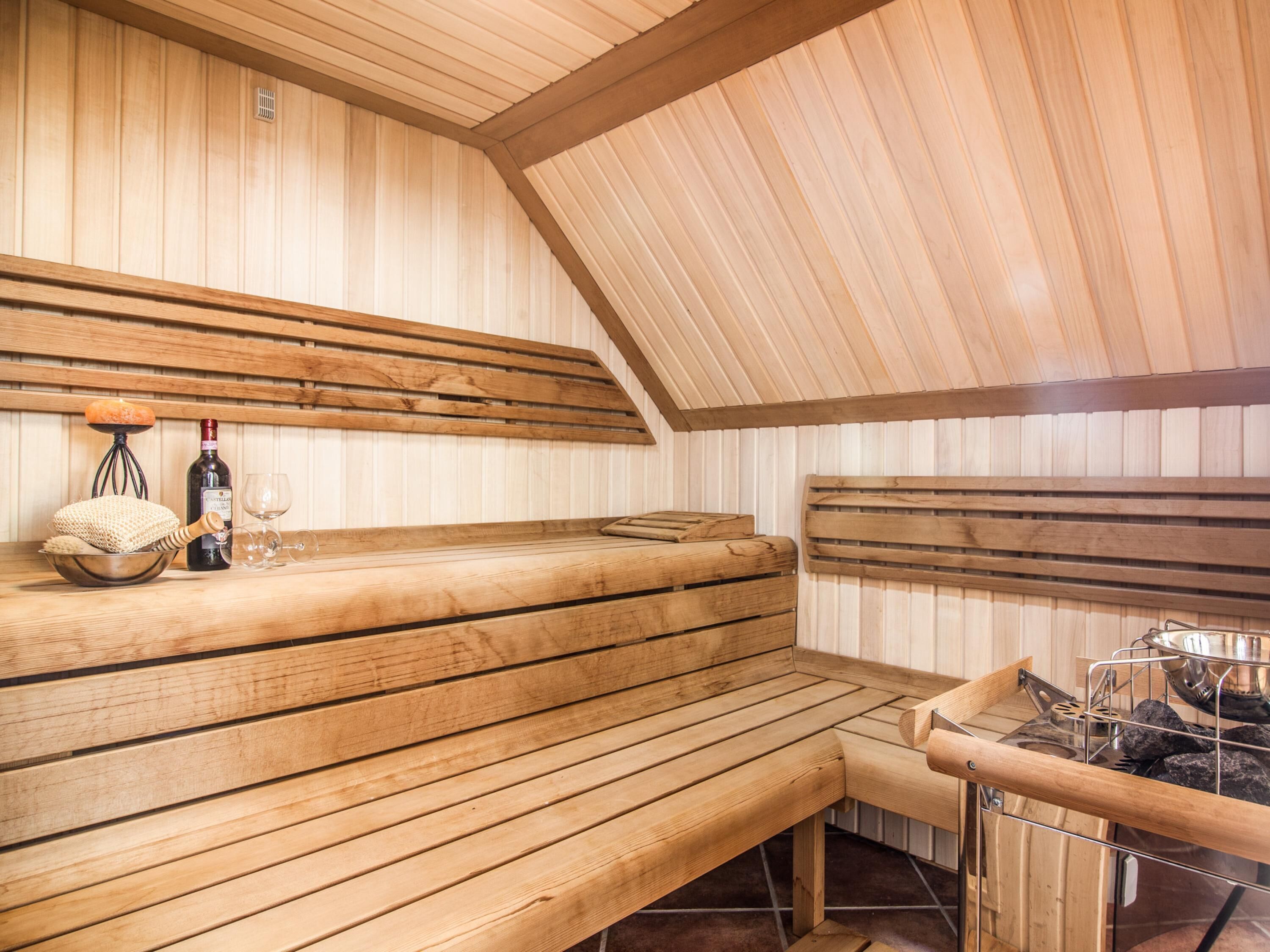 Un sauna avec des bancs en bois, une petite table avec une bouteille et des verres, et un appareil de chauffage pour sauna.