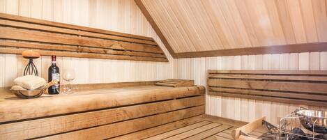 Un sauna avec des bancs en bois, une petite table avec une bouteille et des verres, et un appareil de chauffage pour sauna.