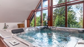 Een bubbelbad in een ruimte met grote ramen, een houten plafond en uitzicht op bomen.