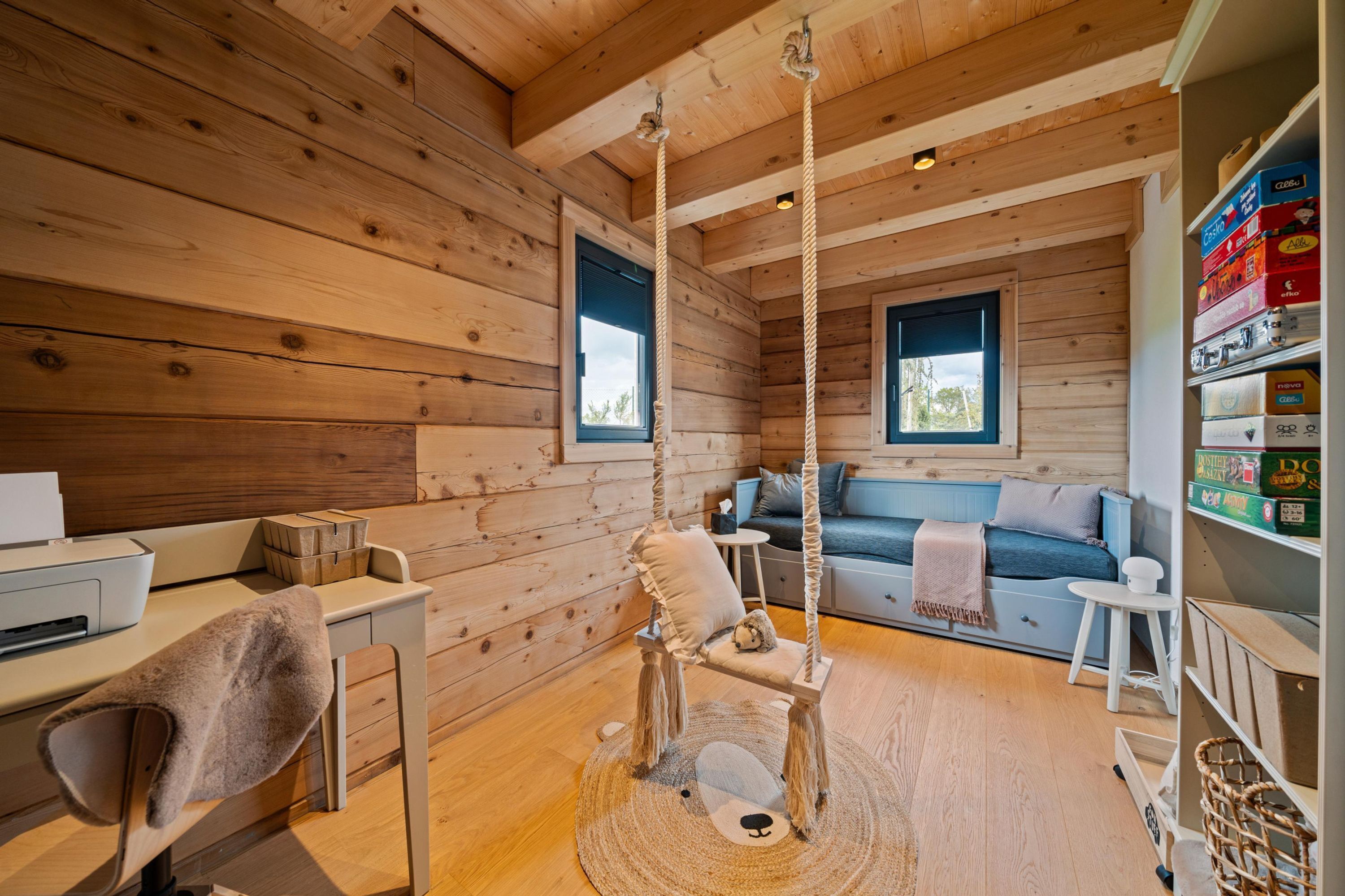 A cozy cabin interior with a wooden interior, a sofa, a desk with a chair, and a hanging chair.
