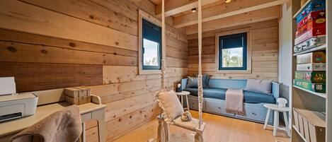 A cozy cabin interior with a wooden interior, a sofa, a desk with a chair, and a hanging chair.