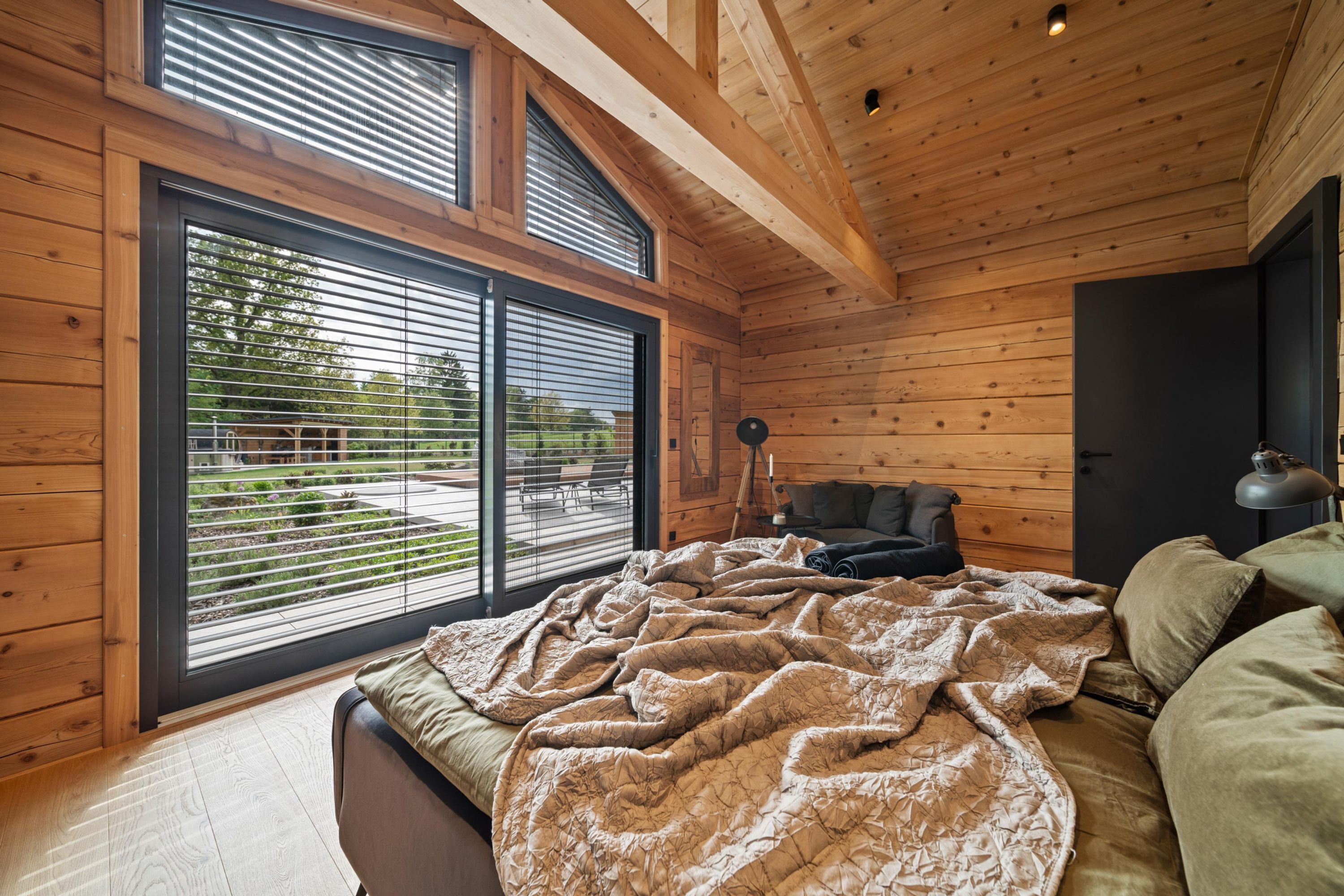A bedroom with a large bed, wooden walls, and a view through large windows.
