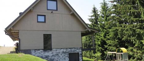 A modern two-story house with a sloped roof, a stone foundation, and a small front porch.