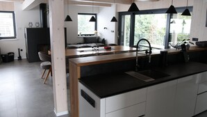 A modern kitchen with a central island, black pendant lights, and a view of a balcony.