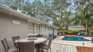 Une terrasse couverte avec une piscine, des meubles en osier et une pancarte sur laquelle on peut lire : « ICI, C’EST NOTRE PETIT COIN DE PARADIS ».