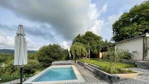 Una terraza de madera con piscina, rodeada de follaje y vistas al campo.