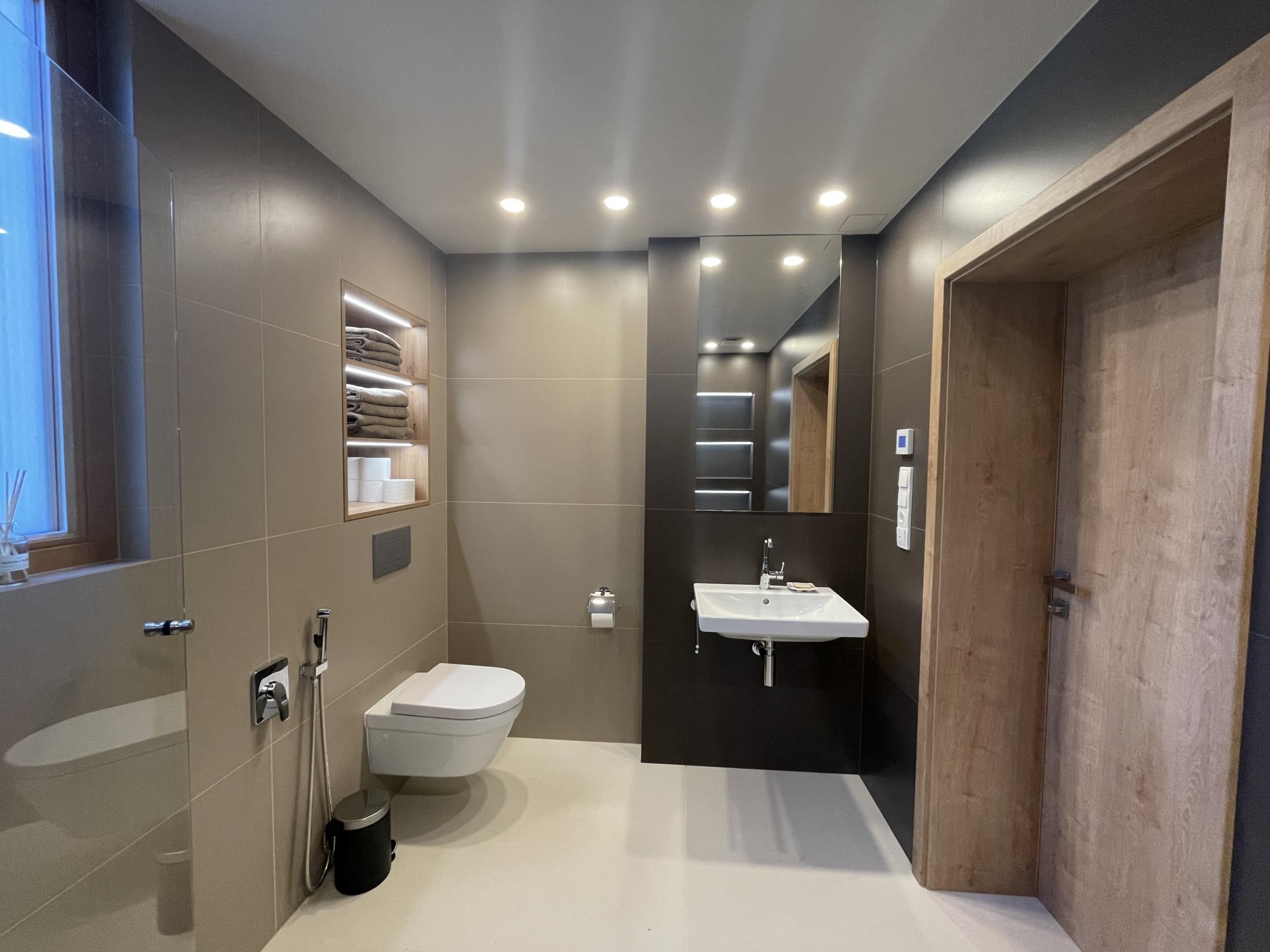A modern bathroom with a toilet, sink, and built-in shelves.