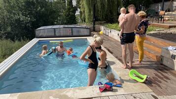 Una piscina con muelle de madera, rodeada de árboles y una casa.