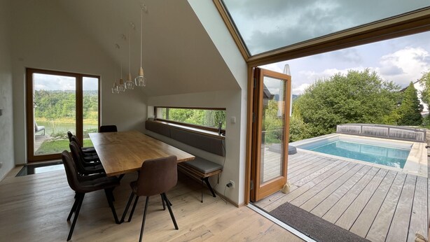 Un comedor moderno con una mesa y sillas de madera, ventanas amplias y vistas a una piscina.