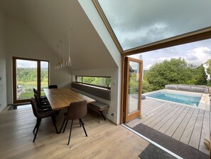 A modern dining area with a wooden table and chairs, large windows, and a view of a swimming pool. - Villa Kretin Vlv142 in Lazinov (Lazinov)