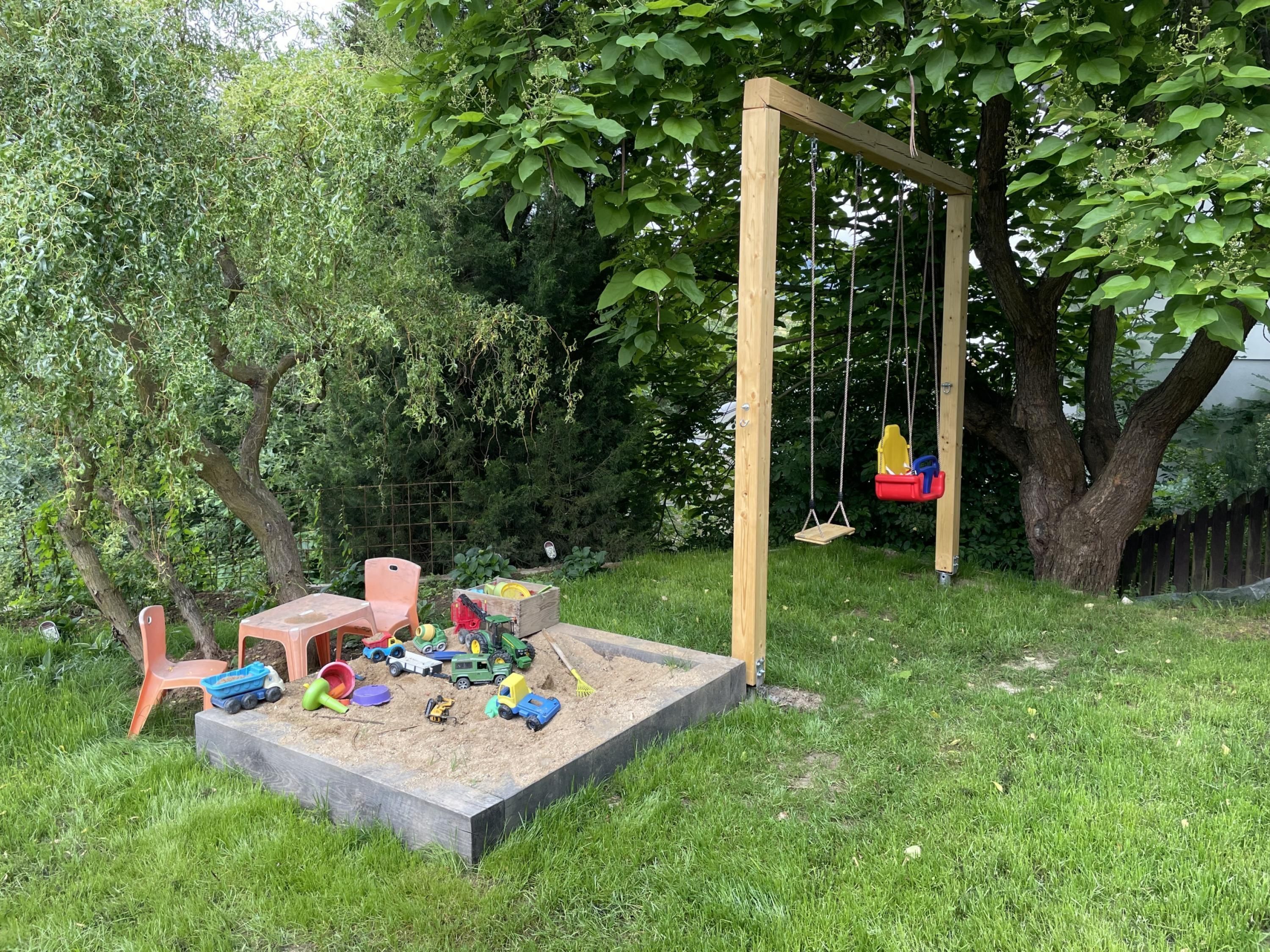 Een speeltuin met een schommel, zandbak en diverse speelgoed.