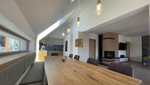 Una sala de estar moderna con una mesa de comedor de madera, asientos cómodos, una chimenea y una cocina al fondo.