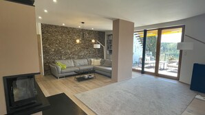 Una sala de estar moderna con un sofá seccional, una chimenea, una pared de piedra y vistas a un balcón con mobiliario exterior.