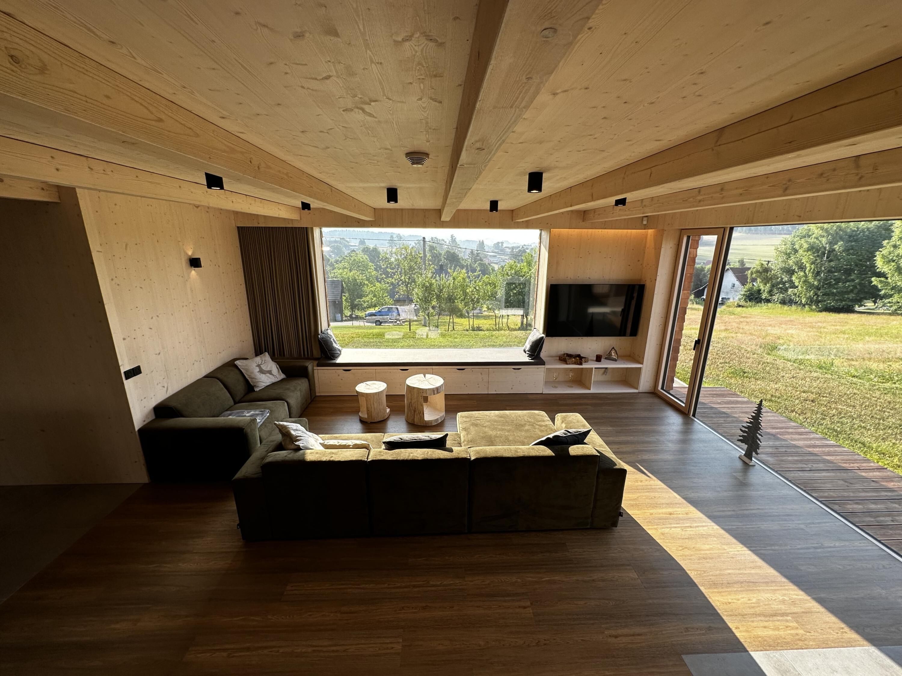 Una sala de estar moderna con un ventanal grande, un sofá, un televisor y techo de madera.