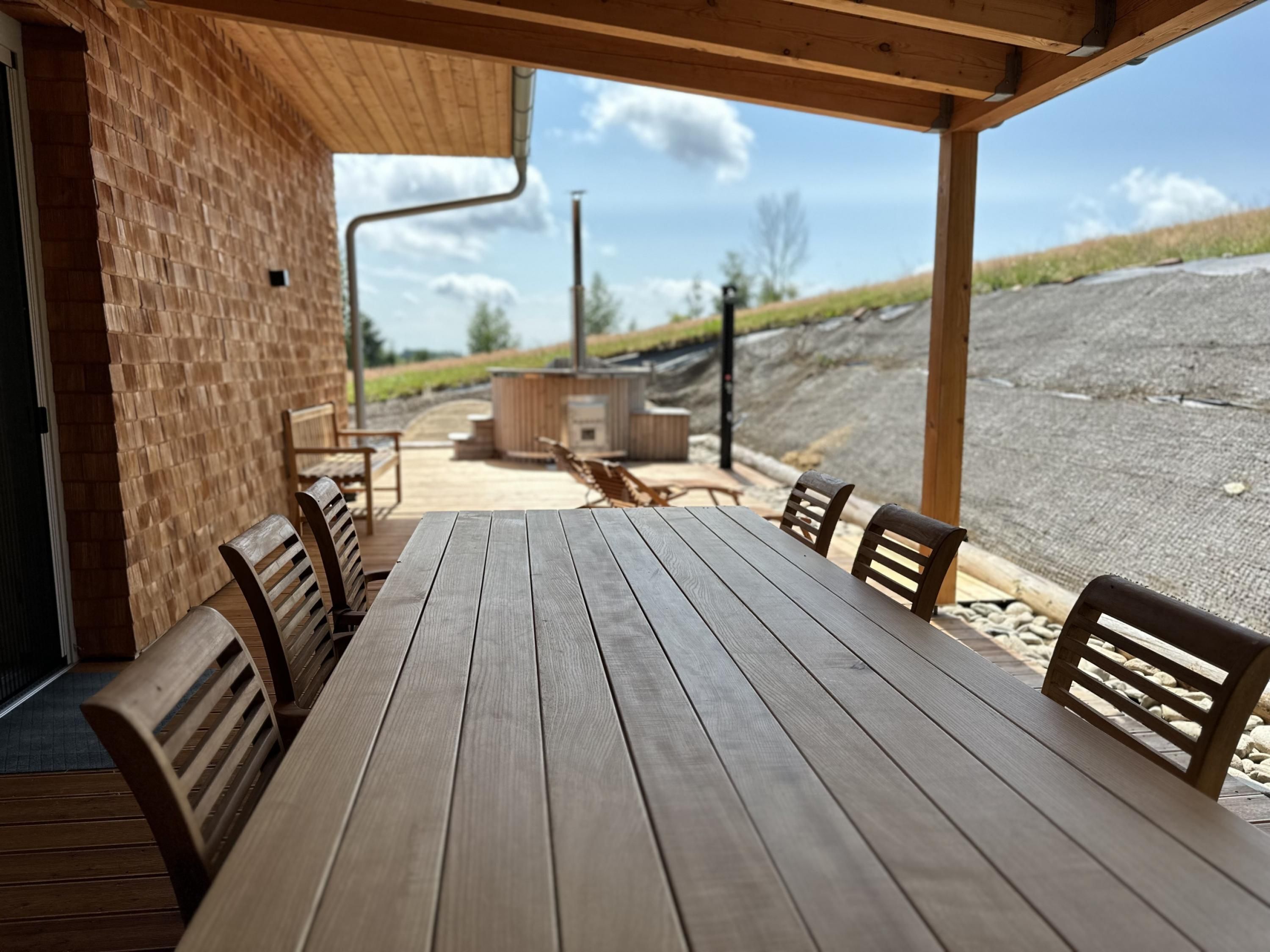 A wooden table and chairs under a covered area with a brick wall, outdoor seating, and a view of the landscape.