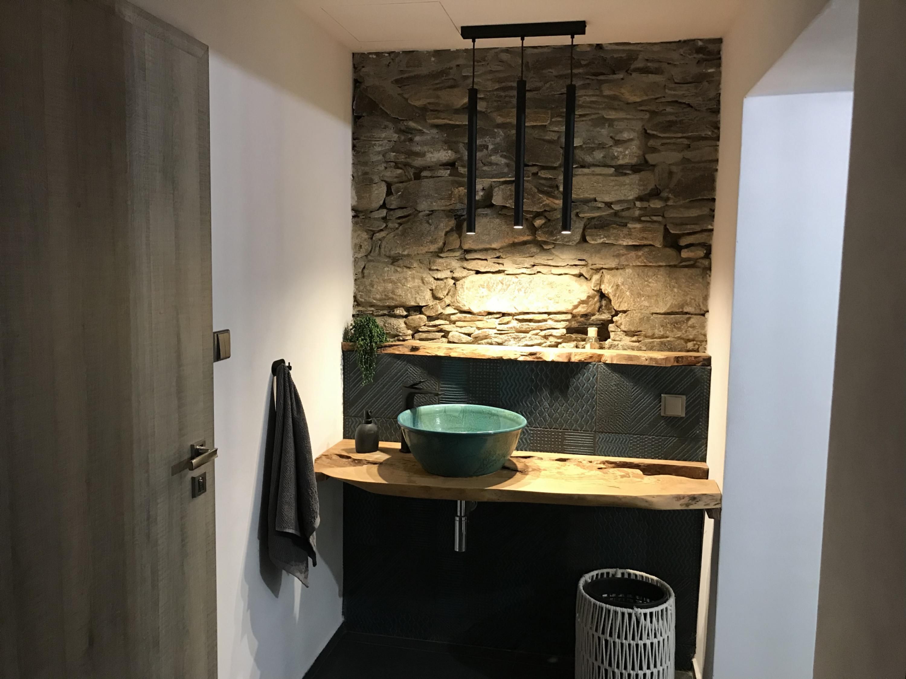 A bathroom with a stone wall, a wooden countertop, a sink, and a hanging towel rack.