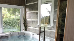 Un baño moderno con una bañera de hidromasaje con mampara de vidrio, un taburete de madera y vistas al exterior.
