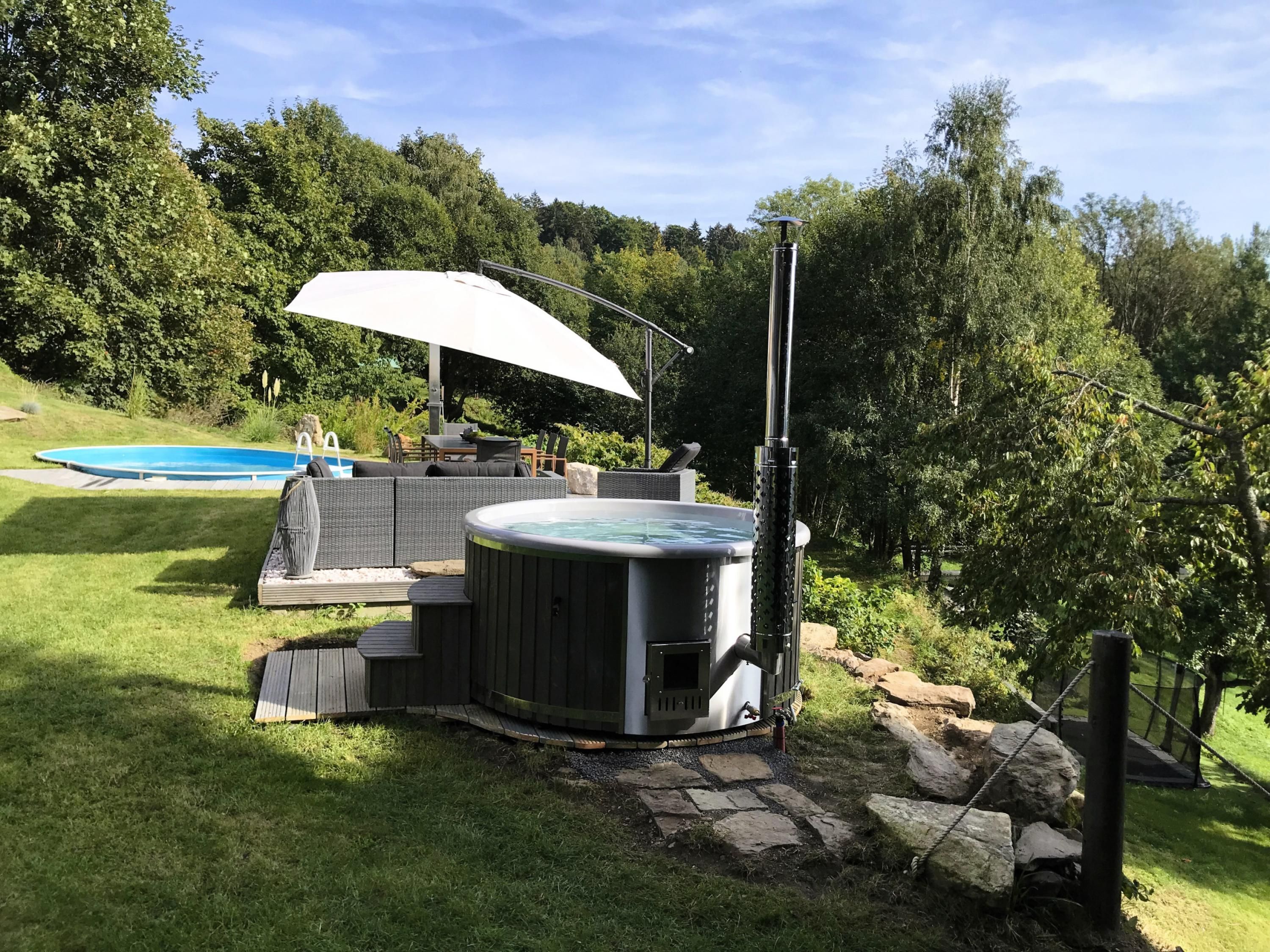 A hot tub with a patio area, a pool, and a covered seating area in a backyard setting.