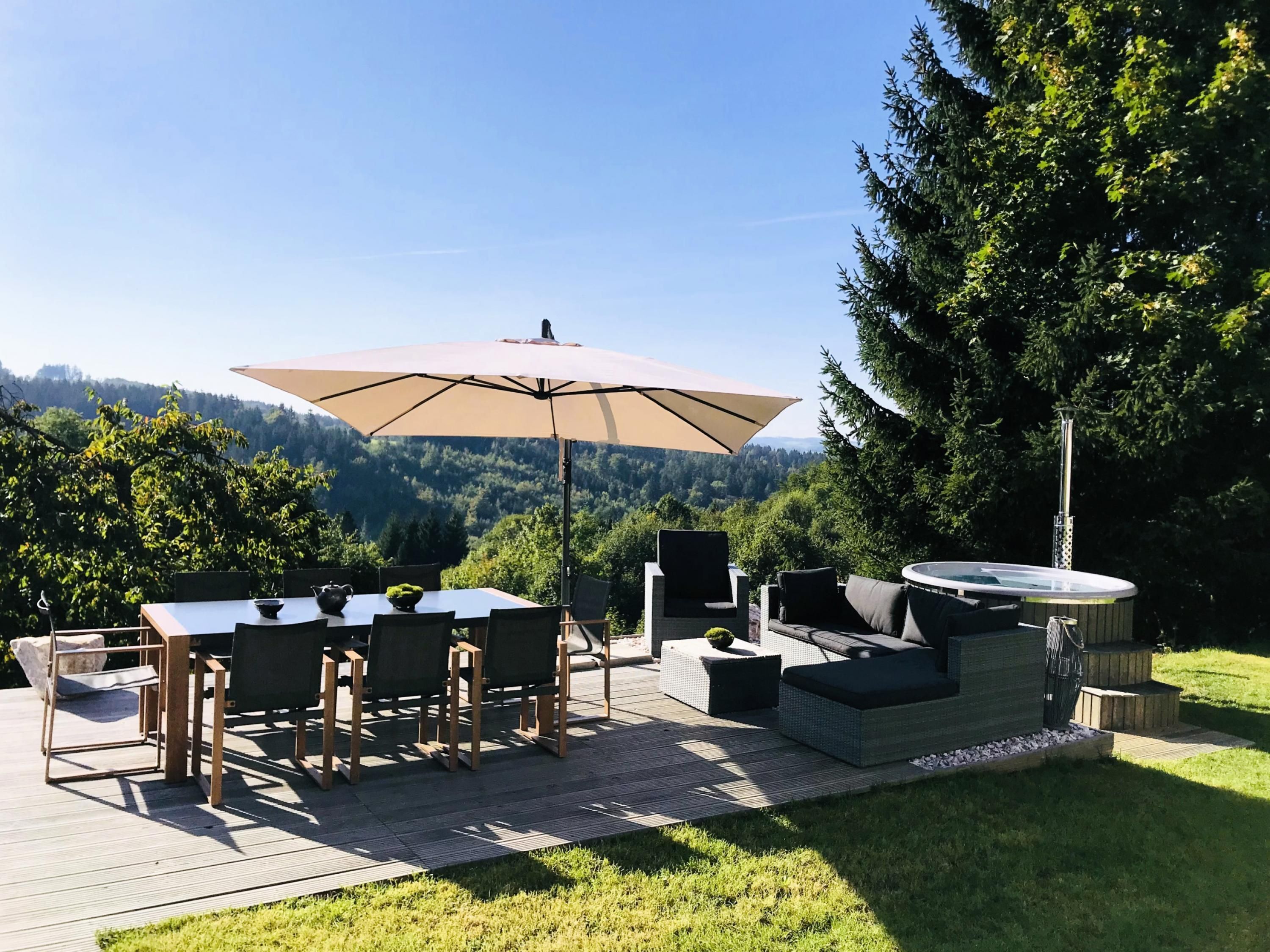 Eine Außenpatio mit Tisch und Stühlen, einem großen Sonnenschirm und einer eingebauten Sitzgruppe mit Whirlpool.