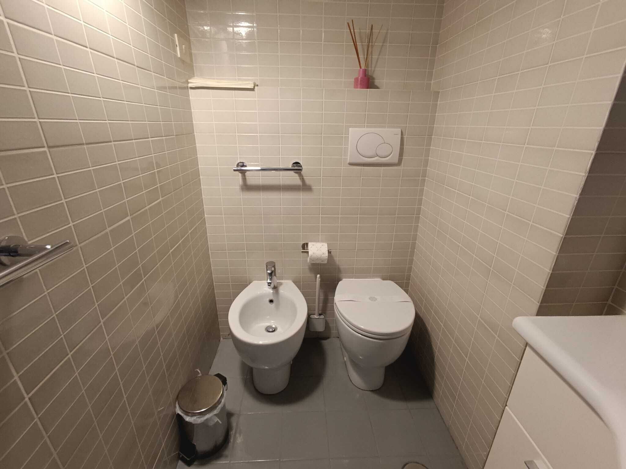 Un baño pequeño con azulejos, un bidé, un inodoro y un cubo de basura.
