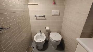 Un baño pequeño con azulejos, un bidé, un inodoro y un cubo de basura.