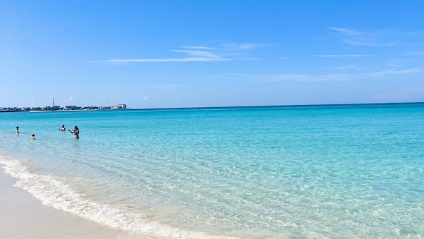 A beach with clear turquoise water, a sandy shore, and a few people in the water. - WOW STYLISH! Next2Bahamar: Pickleball, PrvPool, HotTub + Beachlife & Restaurants (Nassau)