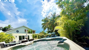 A pool area with lounge chairs and umbrellas, surrounded by palm trees and a house in the background. - WOW STYLISH! Next2Bahamar: Pickleball, PrvPool, HotTub + Beachlife & Restaurants (Nassau)