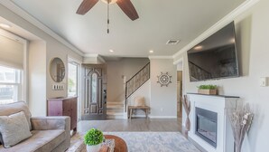 Una sala de estar con sofá, mesa de centro, chimenea, televisor y escalera.