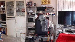 Una habitación con escritorio, silla, televisor, estanterías con varios objetos y un armario.