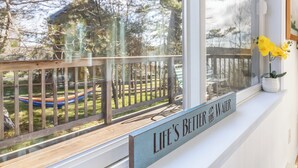 Et vindue med gelænder af træ, en hængekøje og et skilt med teksten 'LIFE'S BETTER ON THE WATER'.