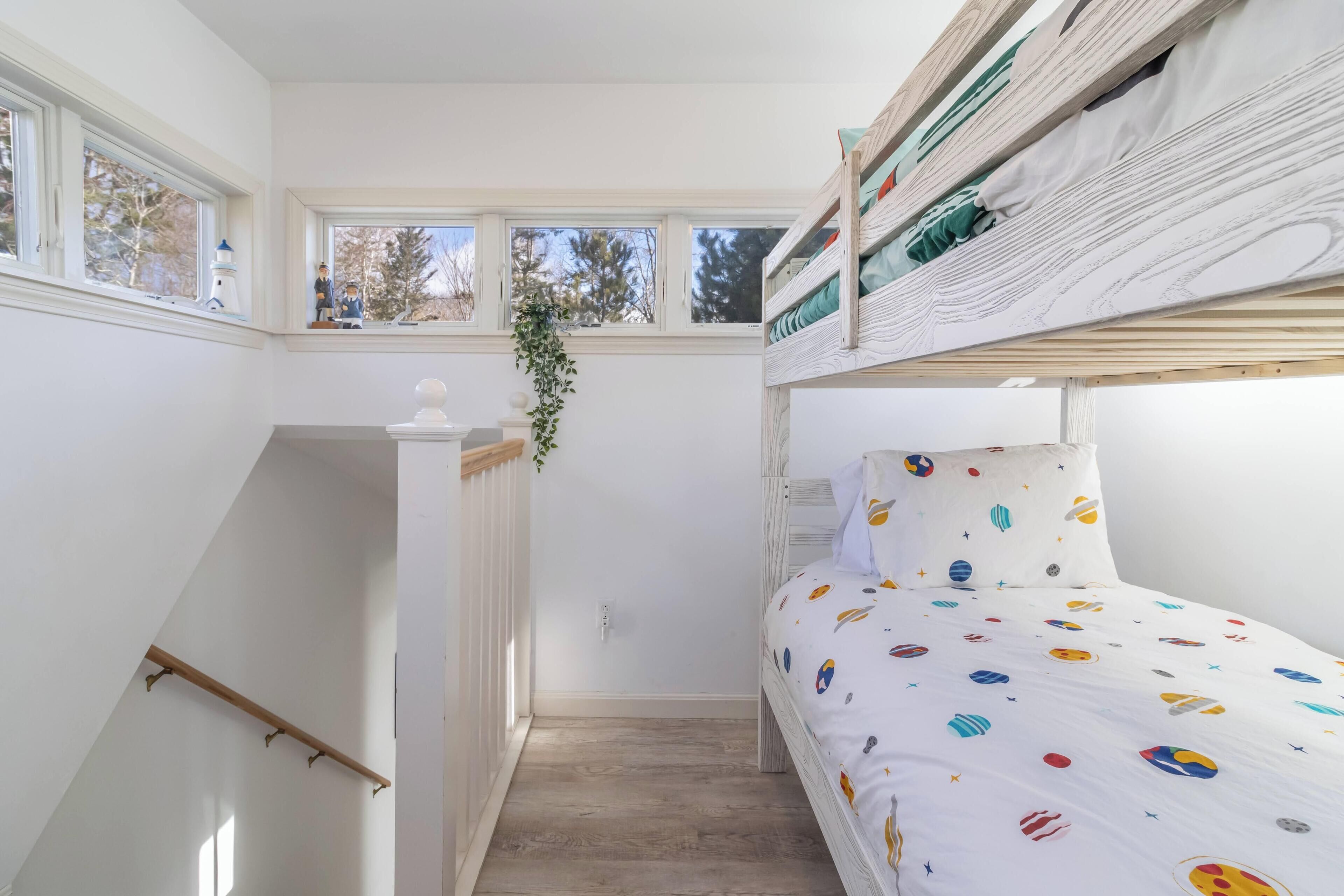 Ein Schlafsaalzimmer mit Etagenbetten, einer kleinen Treppe und einem Fenster mit Blick auf Bäume.