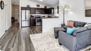A modern living room with a grey sofa, a coffee table, and a kitchen area with dark cabinets and stainless steel appliances. - A Dark Siders dream in Vader's Vacation Villa.  (Davenport)
