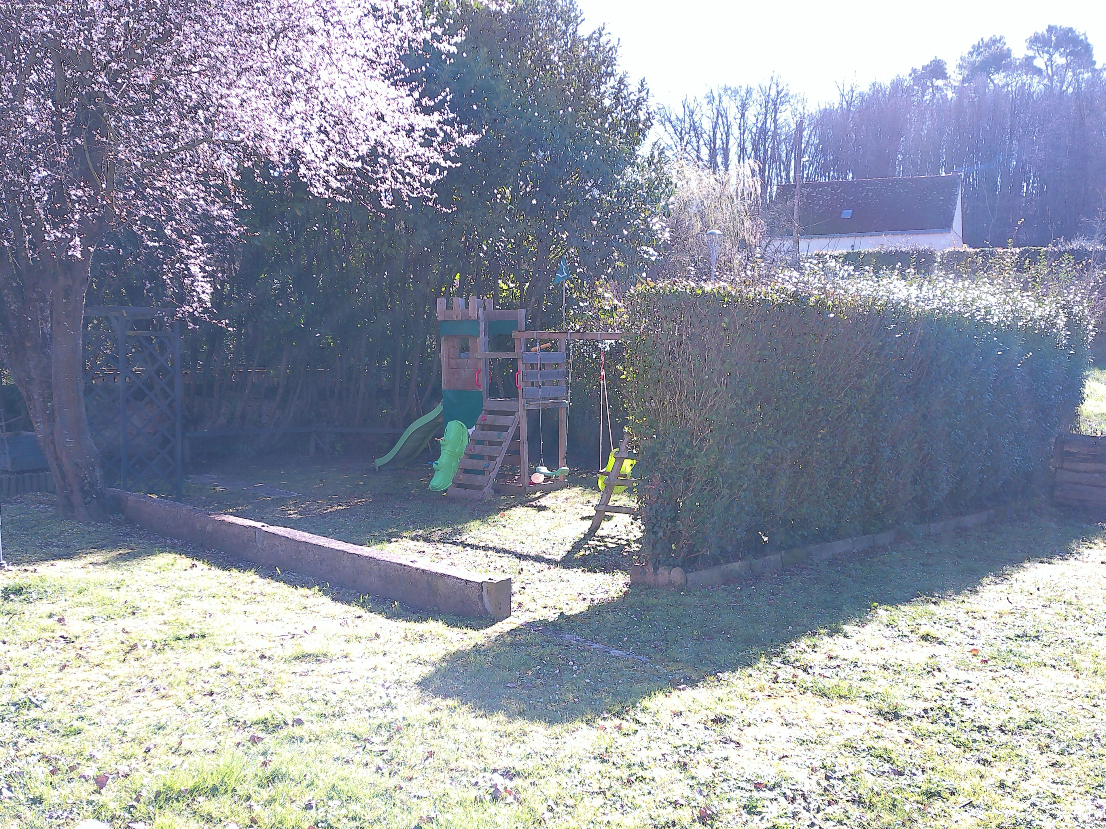 Ein Spielplatz mit Rutsche und Klettergerüsten, umgeben von einem Hecken und Bäumen.