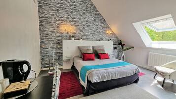 A modern bedroom with a stone wall, a bed with red and blue bedding, a white chair, and a skylight.