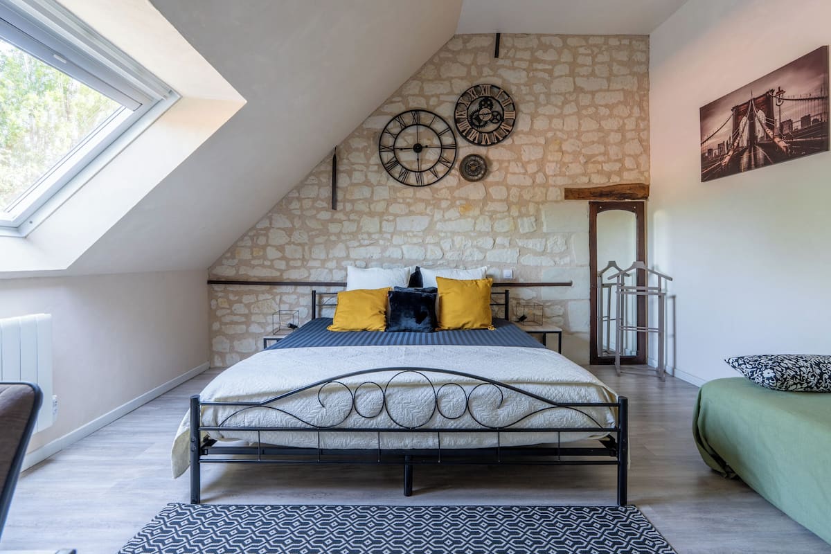 A bedroom with a sloped ceiling, stone wall, a bed with a metal frame, and a skylight.